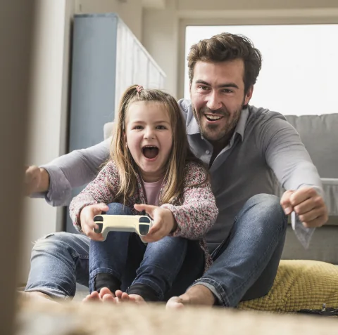 Father and daughter laughing while playing video games together on the sofa
